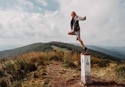 A boy taking a leap of faith. He is jumping off a state border post on top of a mountain range.